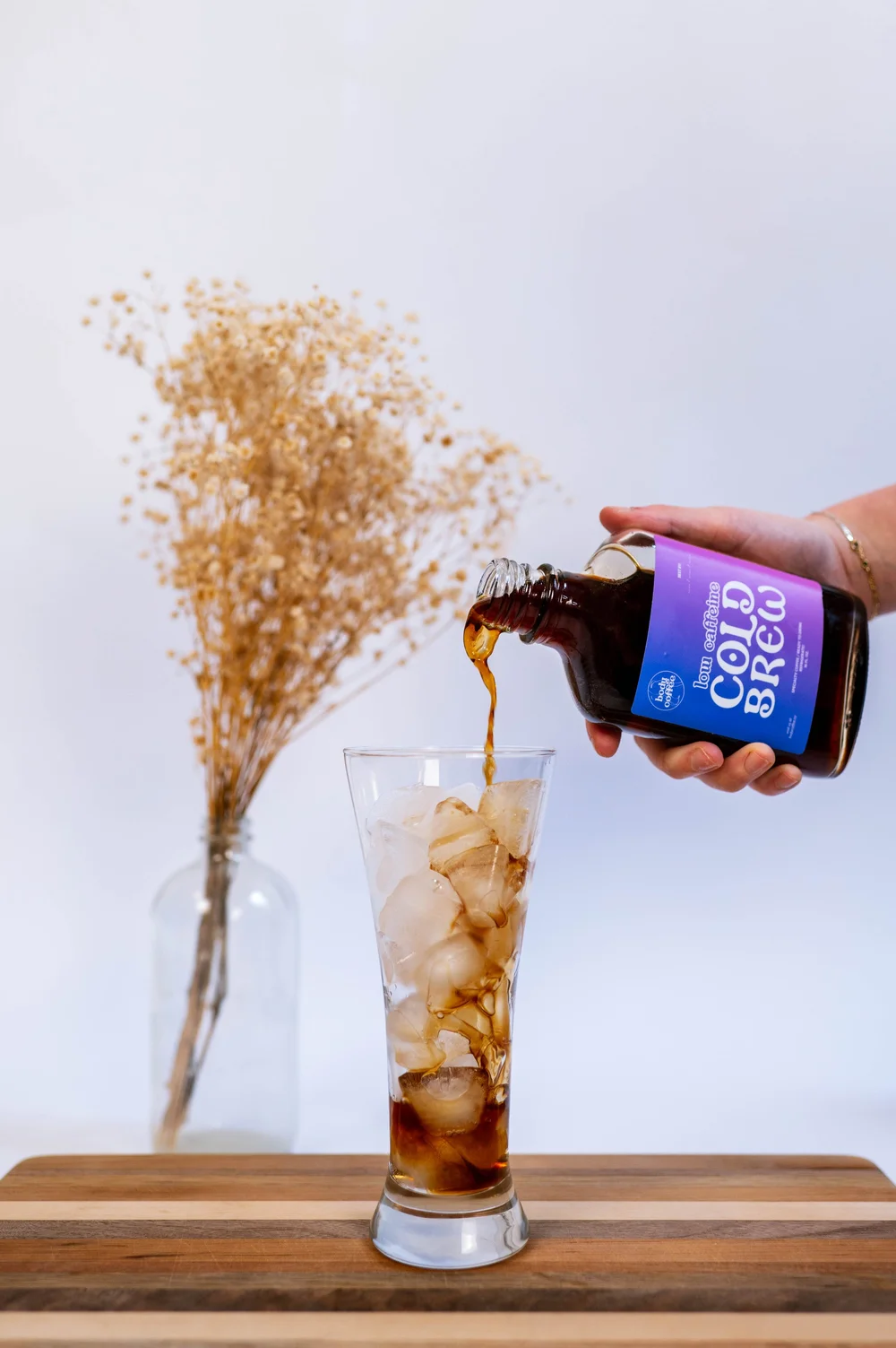 Cold brew pouring into a glass of ice next to dried flowers